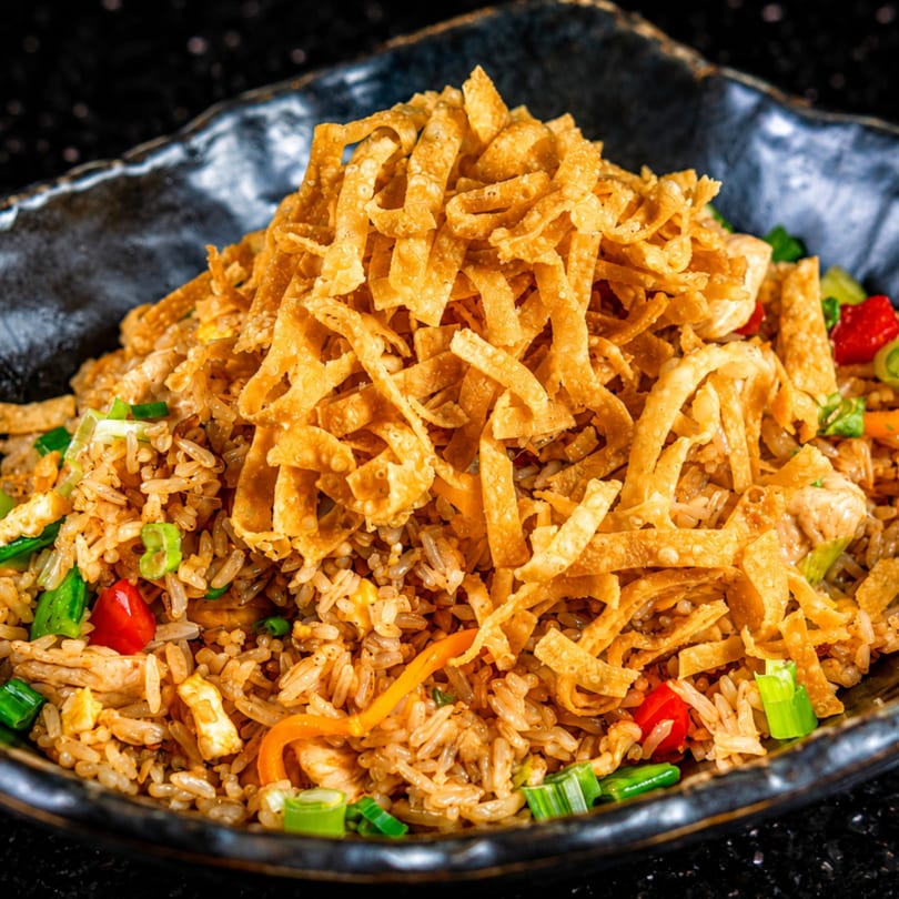 Close-up of fried rice topped with crispy wonton strips, green onions, and red peppers.