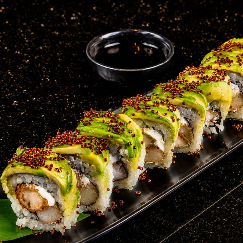 Avocado sushi rolls with crispy shrimp, cream cheese, and quinoa on a black plate with soy sauce.