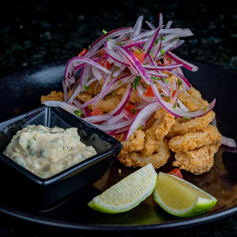 Crispy fried calamari topped with red onions and tomatoes, served with a creamy dip and lime wedges.